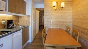 Una cocina con armarios de madera, una estufa, una cafetera y un comedor con mesa y sillas de madera.