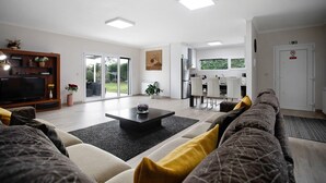 A modern living room with a sofa, coffee table, TV, and a dining area with chairs.
