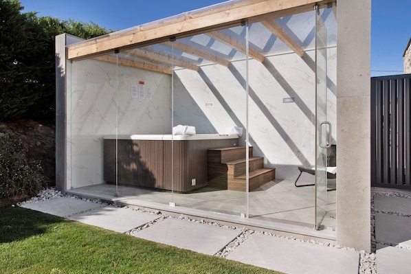 Un espace moderne pour jacuzzi extérieur, doté d’une enceinte en verre, d’escaliers en bois et d’une chaise en métal.
