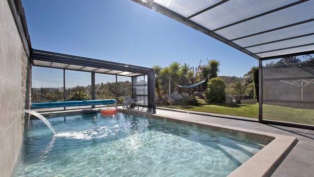 A modern outdoor swimming pool with clear water, surrounded by a glass enclosure, and a view of a natural landscape.