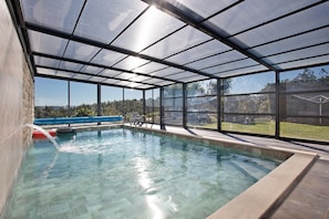 Une piscine dotée d’une enceinte en verre, avec une eau cristalline et une vue sur l’extérieur.