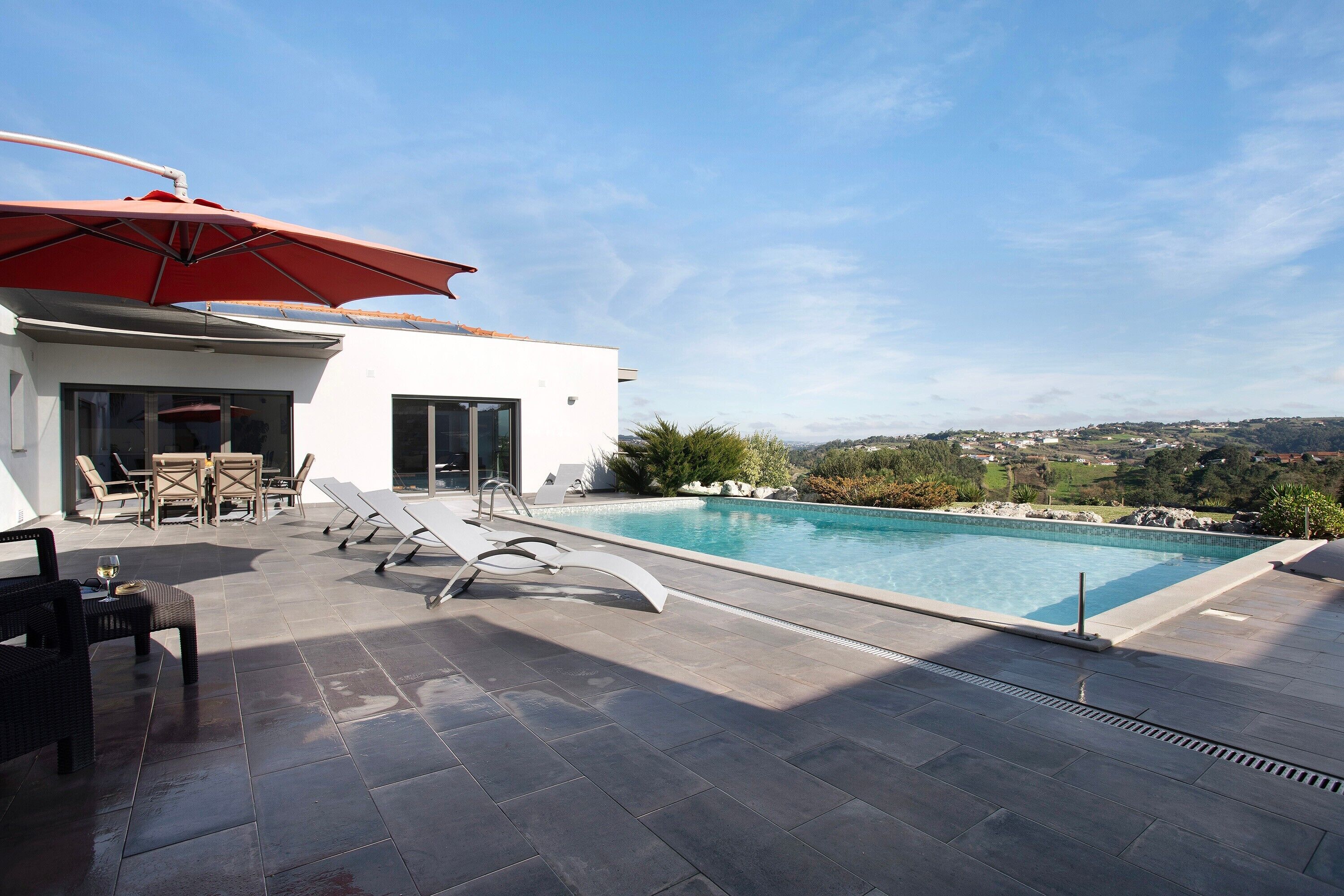 Una piscina en la azotea con vistas al campo, un espacio de descanso techado y un edificio moderno.