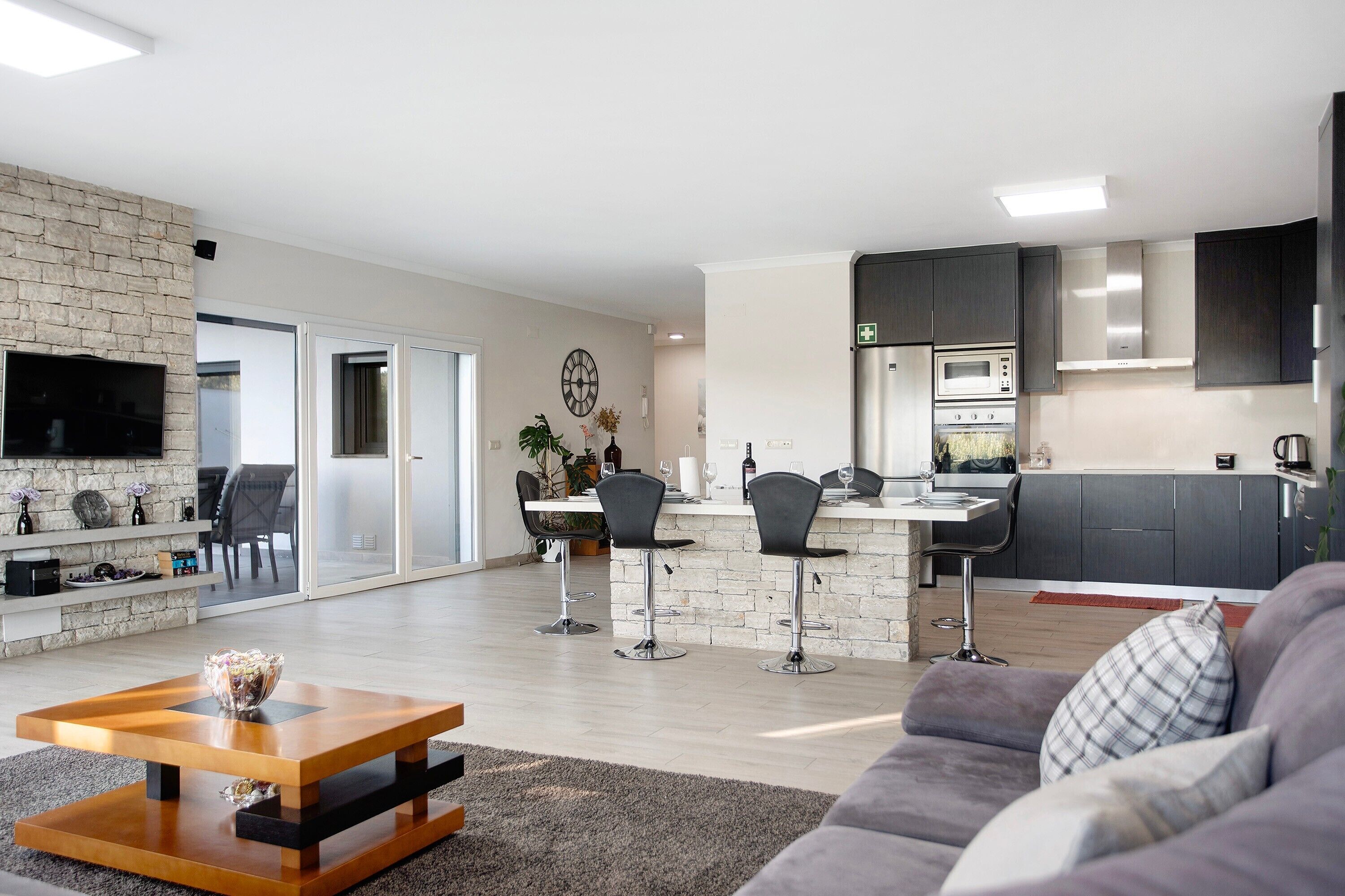 Una sala de estar moderna con un sofá, una mesa de centro y un televisor. Cuenta con una zona de cocina con refrigerador, microondas y armarios.