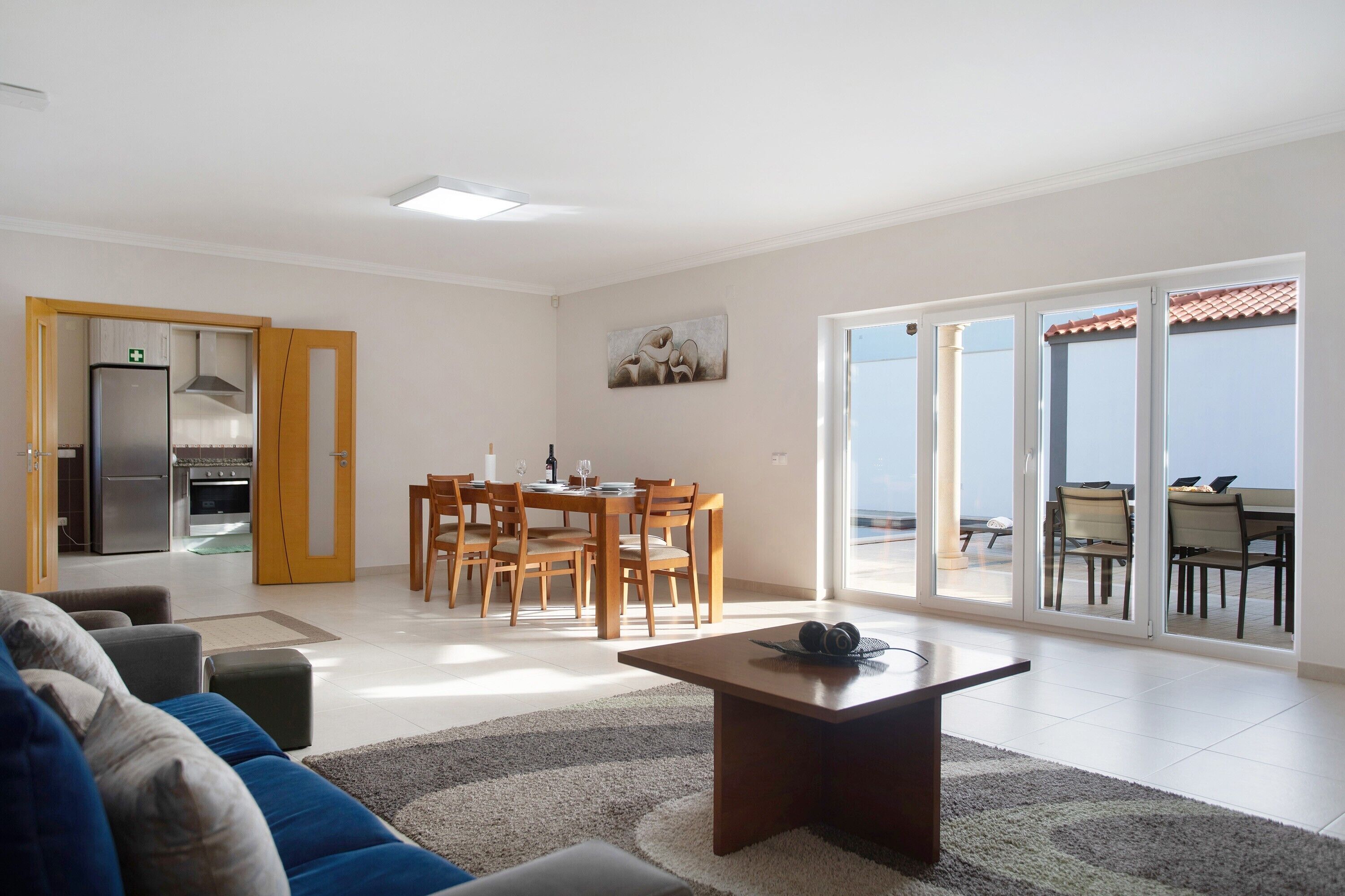 Una sala de estar con un sofá, una mesa de centro y un comedor con sillas y una mesa. Se ve una cocina a través de un umbral abierto.