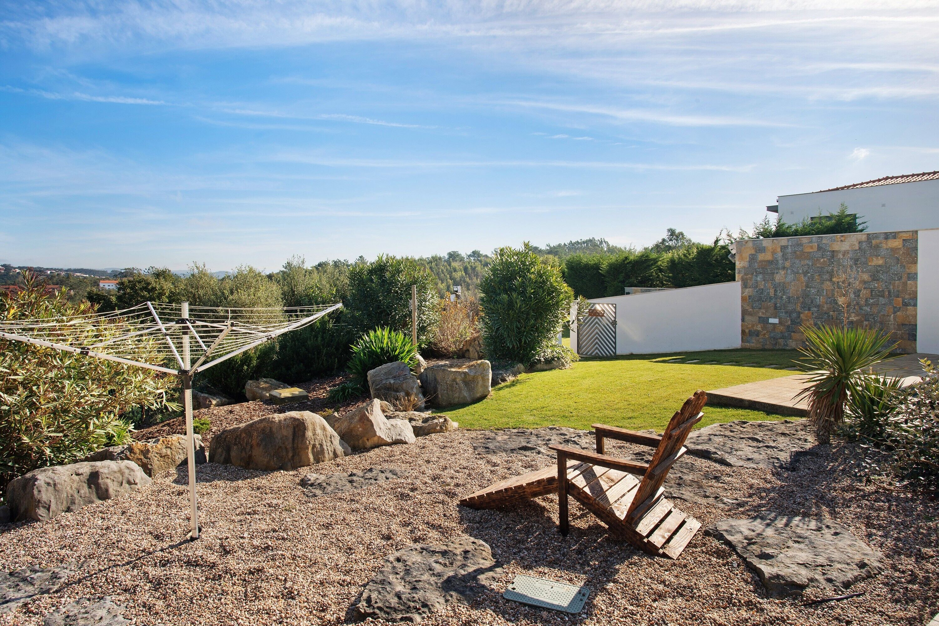 A patio with a wooden chair, a metal umbrella, and a stone wall.