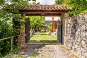 An entrance with a tiled roof, a stone wall, and a gate leading to a courtyard with potted plants and a building in the background. - Holiday Home 'Seaview Camaiore' with Sea View, Private Pool and Wi-Fi (Camaiore)