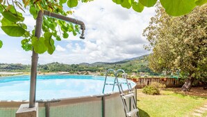 An outdoor swimming pool with a ladder, surrounded by grass and trees, with a view of hills in the background. - Holiday Home 'Seaview Camaiore' with Sea View, Private Pool and Wi-Fi (Camaiore)