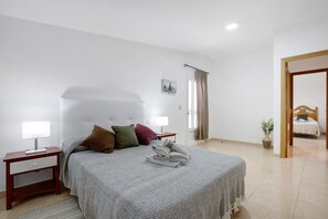 A bedroom with a bed, two bedside tables, a nightstand, a window with curtains, and a door leading to another room. - Vacation Home "Casa Cactus" with Mountain View, Private Terrace & Wi-Fi (Antigua)