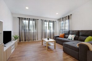 A modern living room with a flat-screen TV, a sofa, a coffee table, and large windows with curtains. - Vacation Home "Casa Cactus" with Mountain View, Private Terrace & Wi-Fi (Antigua)