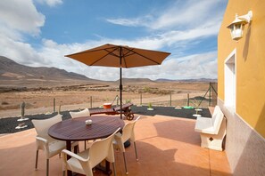 An outdoor patio with a table and chairs, a wooden bench, and a large umbrella. - Vacation Home "Casa Cactus" with Mountain View, Private Terrace & Wi-Fi (Antigua)