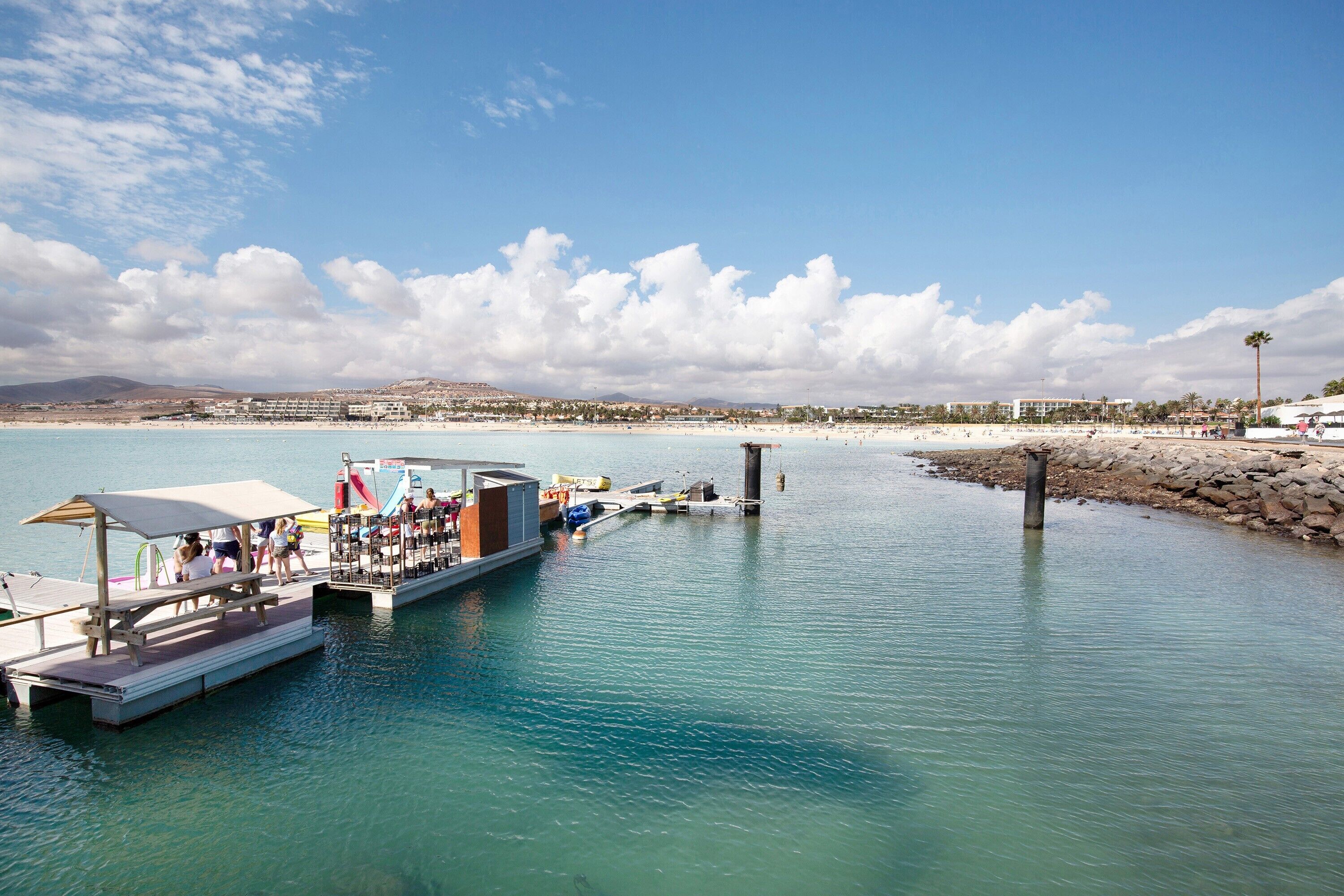 A waterfront hotel with a dock, a pool area, and a beach in the background.