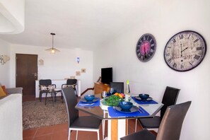 A dining area with a table set for two, chairs, a clock, and a door in the background.