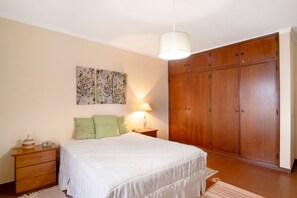A bedroom with a bed, nightstand, lamp, wooden wardrobe, and a wall art piece.