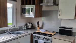 A compact kitchen with a stainless steel microwave, a gas stove, a sink, and a small refrigerator. - Immaculate 8-bed Cabin in Tattershall Lake (Lincoln)