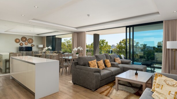 A modern living room with a grey sofa, a coffee table, and a dining area with a table and chairs. - The Warwick 306 (Cape Town)