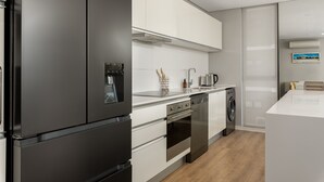 A modern kitchen with a black refrigerator, white cabinets, a built-in oven, and a dishwasher. - The Warwick 306 (Cape Town)