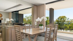 A modern dining area with a wooden table and chairs, a vase of white orchids, and a view of greenery outside. - The Warwick 306 (Cape Town)