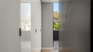 A modern hallway with a wooden floor, white walls, and a large window offering a view of a hillside and buildings. - The Warwick 306 (Cape Town)
