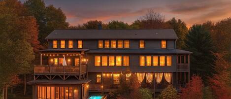 A multi-story wooden house with balconies, a pool, and a view of autumn foliage.