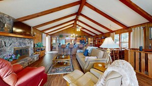 A spacious living room with a fireplace, a kitchen in the background, and a dining area.