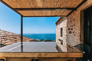 An outdoor terrace with a view of the sea, stone walls, and a wooden table with chairs. - Pyrgos Towers (West Mani)