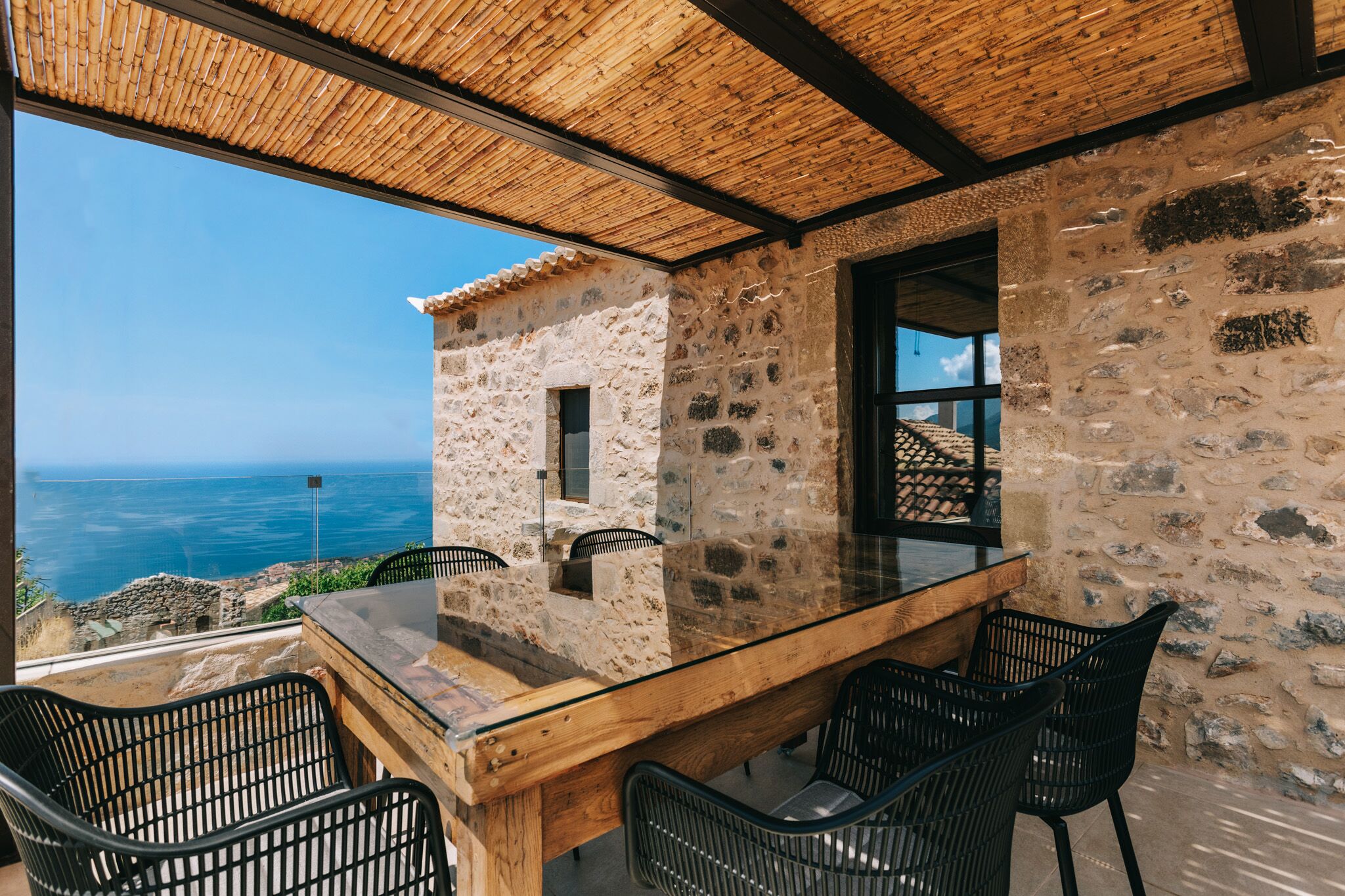 A stone building with a glass table and chairs, overlooking a scenic view.