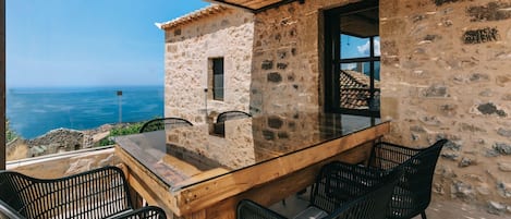 A stone building with a glass table and chairs, overlooking a scenic view.