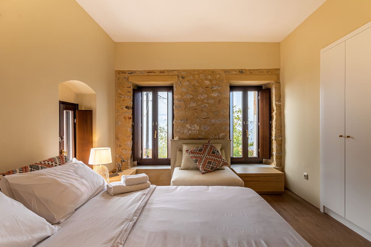 A bedroom with a stone wall, two beds, a window seat, and a wardrobe.