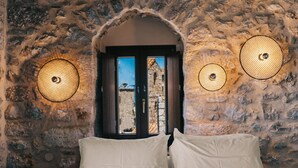 A bedroom with a stone wall, a bed with white and yellow bedding, and two wall-mounted lamps. - Pyrgos Towers (West Mani)