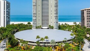 A modern hotel with a circular central courtyard surrounded by palm trees and a beach view. - Beachfront 3BR/3BA condo with heated pool, Wi‑Fi, and full kitchen. (Marco Island)