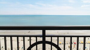 Une vue sur la plage depuis un balcon doté d’une balustrade, avec une plage de sable et l’océan en toile de fond.