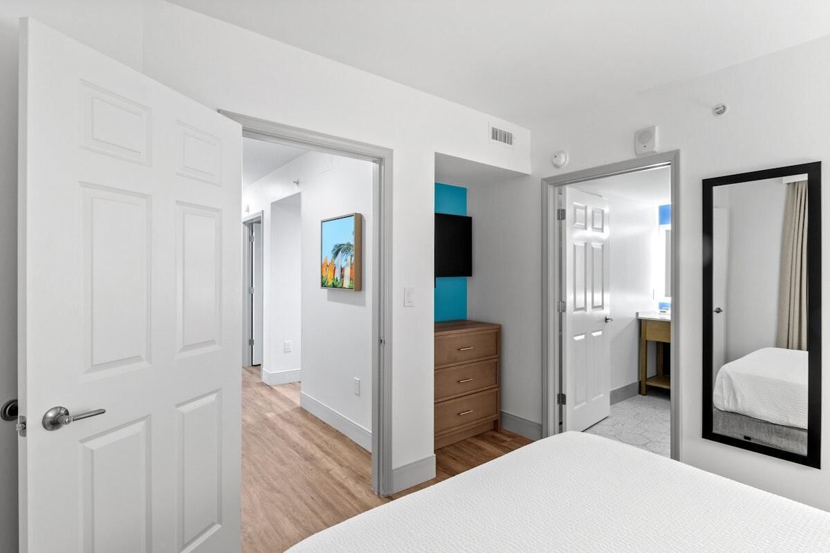 A hotel room with a bed, a dresser, a mirror, and a door leading to another room.