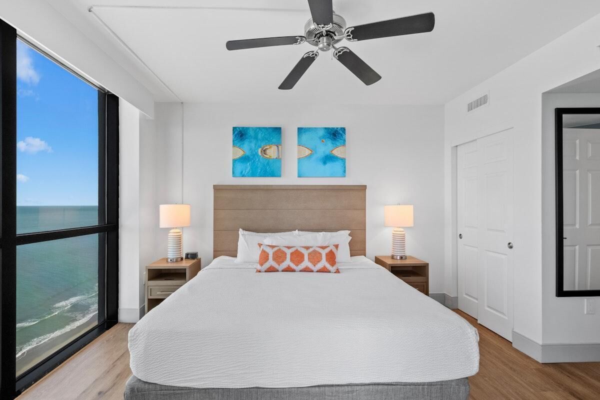 Ein Schlafzimmer mit einem großen Bett, zwei Nachttischlampen, einem Deckenventilator und Bildern an der Wand.