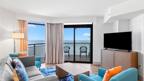 Ein modernes Hotelzimmer mit Balkon, einem Flachbildfernseher und einer Sitzecke.