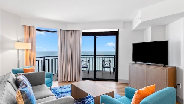 Ein modernes Hotelzimmer mit Balkon, einem Flachbildfernseher und einer Sitzecke.