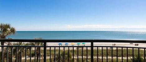 A balcony with a view of the beach and ocean.