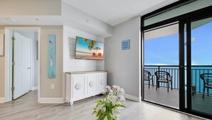 A living room with a view of the ocean, a white console table, a painting, and a vase of flowers.