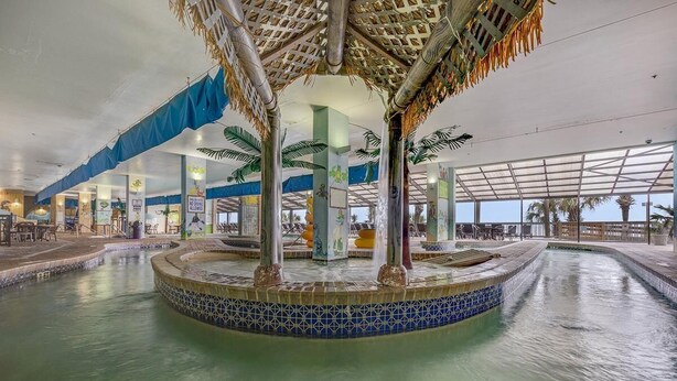 A large indoor pool with a central fountain, surrounded by palm trees and a blue-tiled edge.