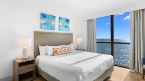 Camera d'albergo con un letto grande, due comodini, vista sull'oceano attraverso un'ampia finestra e due opere d'arte appese sopra il letto.