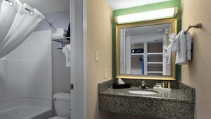 A bathroom with a granite countertop sink, a white toilet, a shower with a white curtain, and a mirror with a gold frame. - Jamaican Building Beachfront Escape & Pool Perks (Myrtle Beach)