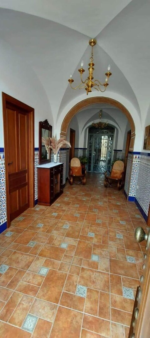 A hallway with tiled flooring, wooden doors, and a chandelier.