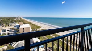 Uitzicht op de kust vanaf een balkon, met een strand en gebouwen op de achtergrond.