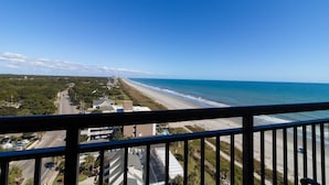 A coastal view from a balcony overlooking a beach and a road with buildings in the distance. - Newly Renovated Ocean View 2 Bdrm Condo 12th Floor (Myrtle Beach)