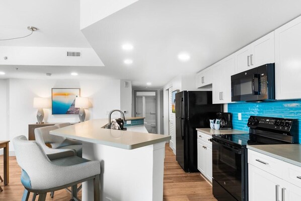 Una cocina moderna con armarios blancos, un refrigerador negro, un horno empotrado y un salpicadero azul.