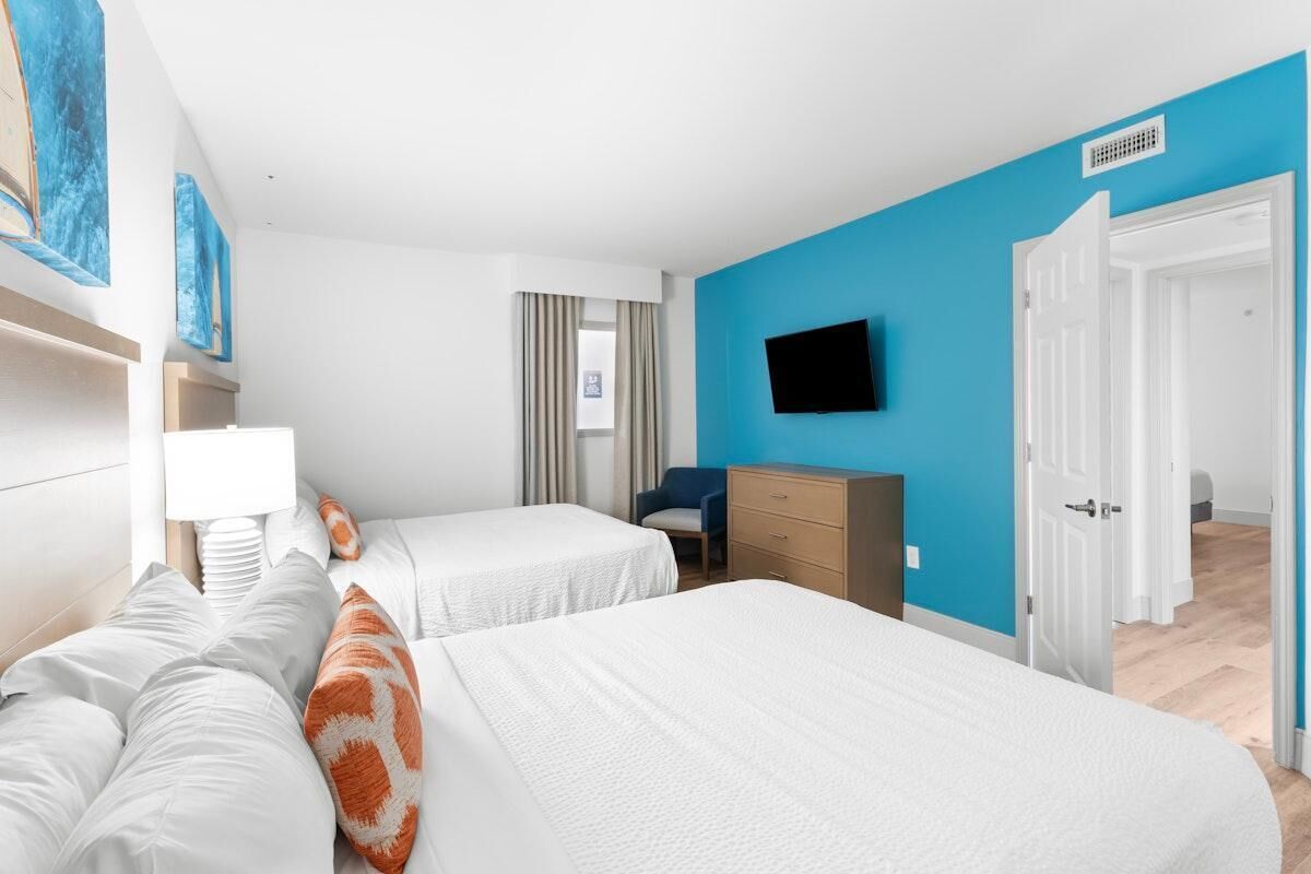 A hotel room with two beds, a TV mounted on the wall, a desk, and a chair.