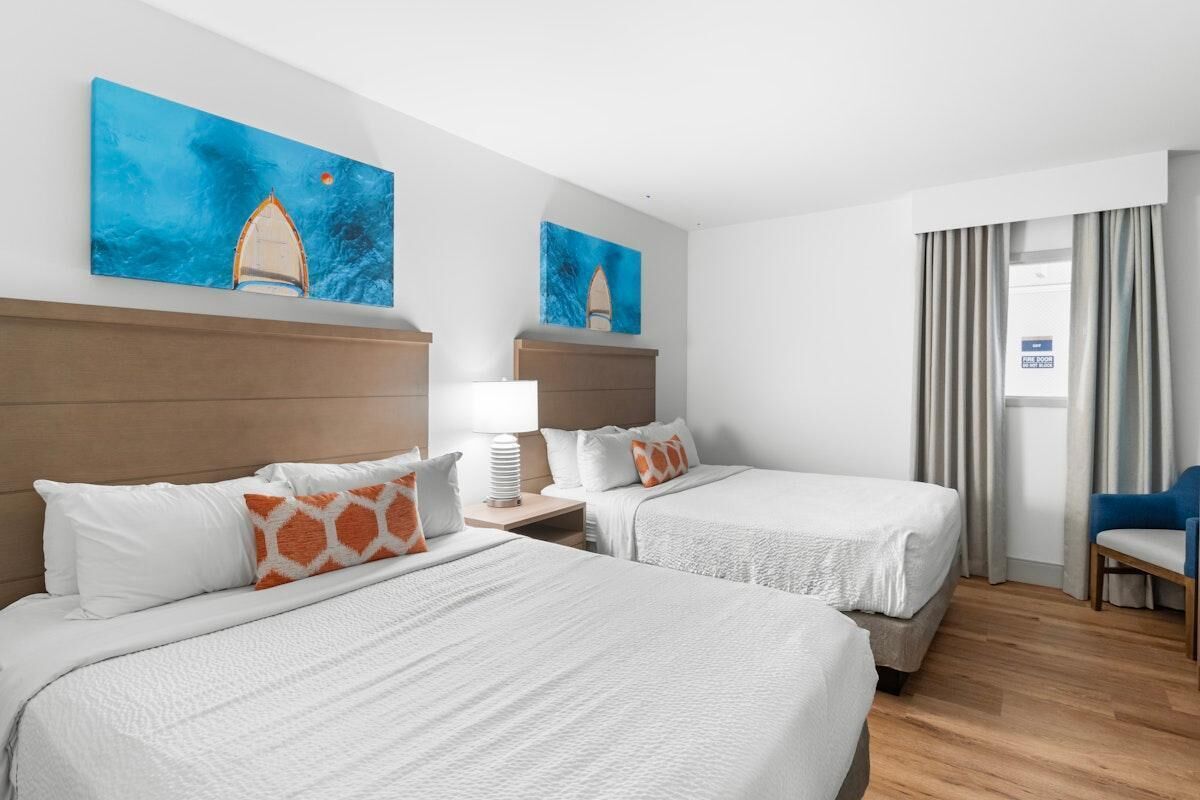 A hotel room with two beds, a nightstand, a lamp, and a chair.