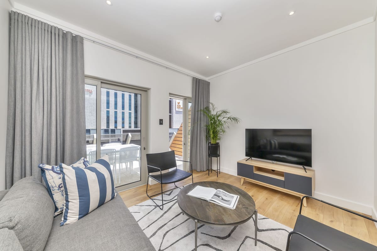 A modern living room with a sofa, a coffee table, a TV, and a balcony with outdoor furniture.