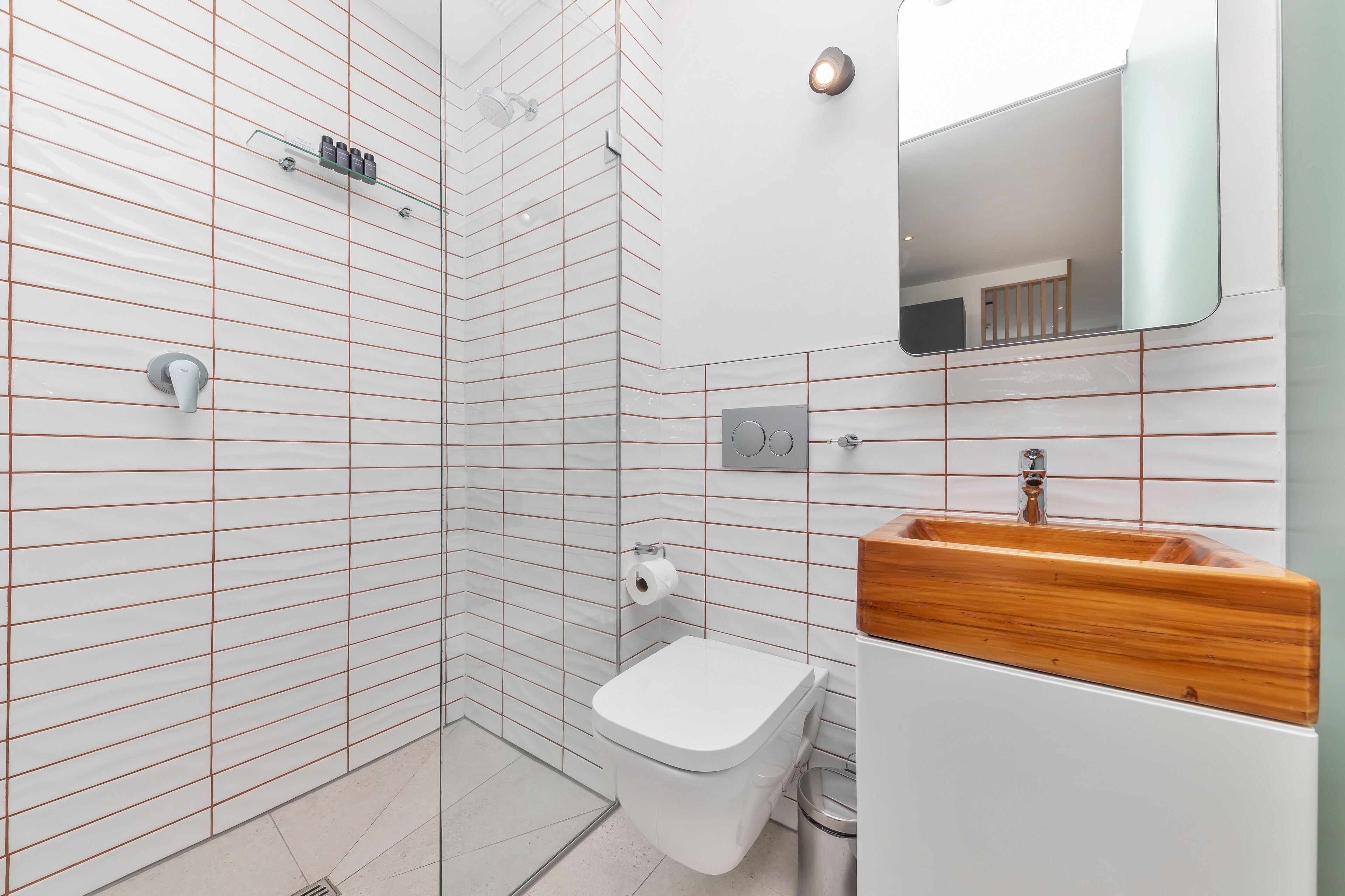 A modern bathroom with a glass shower enclosure, a toilet, a sink with a wooden countertop, and a mirror.