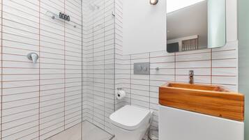 A modern bathroom with a glass shower enclosure, a toilet, a sink with a wooden countertop, and a mirror.