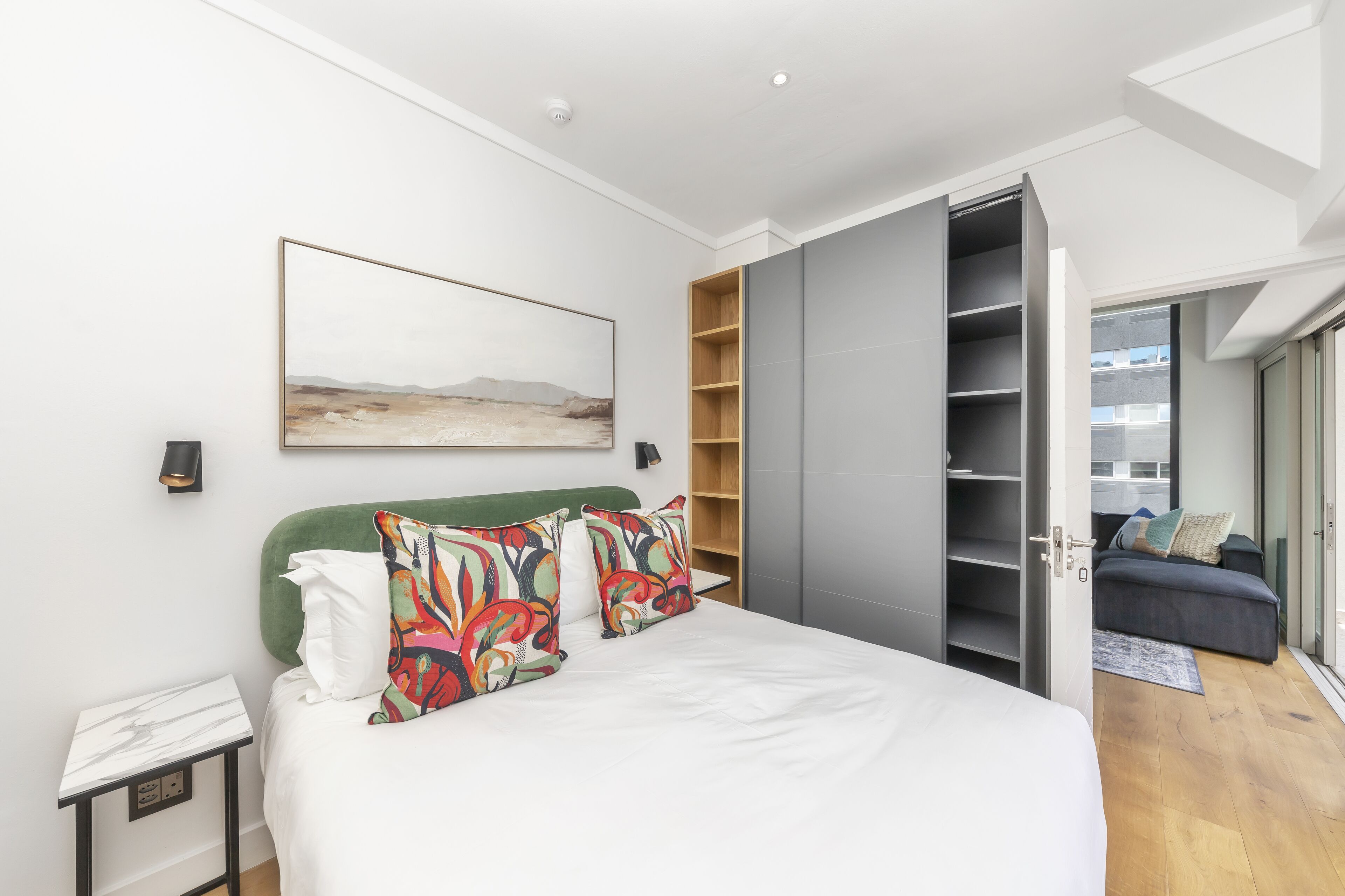 Ein modernes Schlafzimmer mit Bett, einem Bild, einem Kleiderschrank und Blick ins Freie.